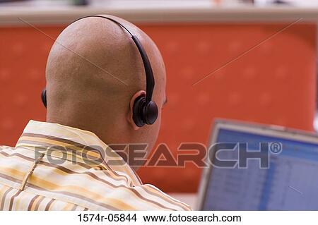 Rear view of a male customer service representative wearing a headset sitting in front of a laptop View Large Photo Image Picture - Rear view of a male customer service representative wearing a headset sitting in front of a laptop. Fotosearch