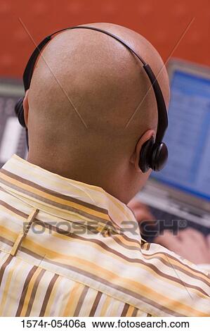 Stock Image - Rear view of a male customer service representative wearing a headset sitting in front of a laptop. Fotosearch