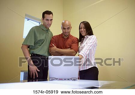 Two businessmen and a businesswoman standing in front of a laptop View Large Photo Image Stock Photo - Two businessmen and a businesswoman standing in front of a laptop. Fotosearch