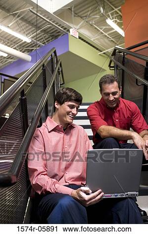 Two businessmen sitting on stairs in front of a laptop View Large Photo Image Stock Image - Two businessmen sitting on stairs in front of a laptop. Fotosearch
