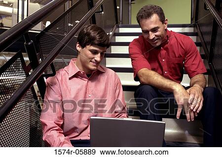 Two businessmen sitting on stairs in front of a laptop View Large Photo Image Stock Photo - Two businessmen sitting on stairs in front of a laptop. Fotosearch