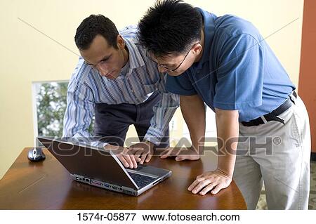 Stock Photo - Two businessmen standing looking at a laptop. Fotosearch