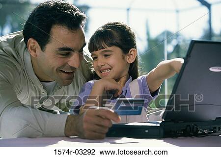 Stock Image - Father and his daughter in front of a laptop holding a credit card. Fotosearch