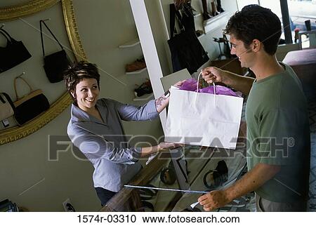 Female sales clerk giving a shopping bag to a young man View Large Photo Image Stock Image - Female sales clerk giving a shopping bag to a young man. Fotosearch