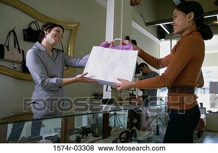 Female sales clerk giving a shopping bag to a young woman View Large Photo Image Stock Photo - Female sales clerk giving a shopping bag to a young woman. Fotosearch