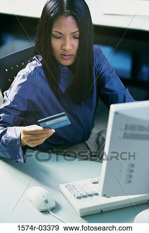 High angle view of a young woman sitting in front of a computer holding a credit card View Large Photo Image Stock Photo - High angle view of a young woman sitting in front of a computer holding a credit card. Fotosearch
