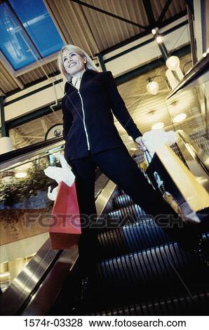 Low angle view of a young woman standing on an escalator View Large Photo Image Stock Photo - Low angle view of a young woman standing on an escalator. Fotosearch