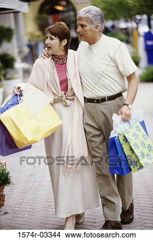Picture - Mature couple carrying shopping bags walking on the sidewalk. Fotosearch