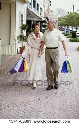 Stock Image - Mature couple carrying shopping bags walking on the sidewalk. Fotosearch