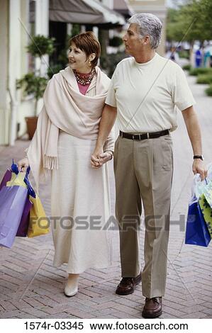 Stock Photography - Mature couple carrying shopping bags walking on the sidewalk. Fotosearch