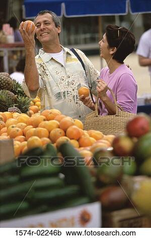 Stock Image - Mature couple picking oranges from shop in a market. Fotosearch