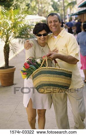 Stock Image - Mature couple walking on the street with a basket of flowers. Fotosearch