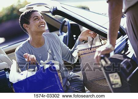 Stock Image - Mature woman sitting in a car carrying shopping bags. Fotosearch