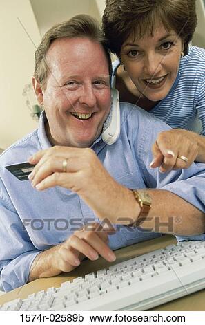 Stock Image - Mid adult couple in front of a computer holding a credit card. Fotosearch