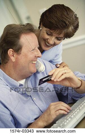 Stock Image - Mid adult couple in front of a computer holding a credit card. Fotosearch