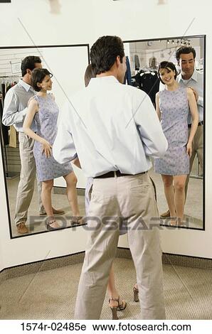 Mid adult couple standing in front of a mirror in the fitting room of a clothing store View Large Photo Image Stock Image - Mid adult couple standing in front of a mirror in the fitting room of a clothing store. Fotosearch