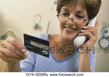 Stock Image - Mid adult woman talking on a cordless phone holding a credit card. Fotosearch