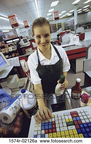 Stock Image - Portrait of a female sales clerk working on a cash register at a supermarket checkout counter. Fotosearch