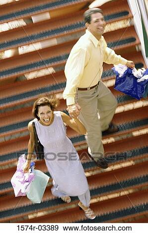 Portrait of a mid adult couple walking down stairs carrying shopping bags View Large Photo Image Stock Photo - Portrait of a mid adult couple walking down stairs carrying shopping bags. Fotosearch