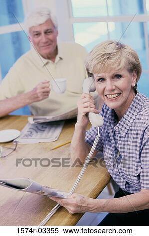 Stock Photography - Portrait of a senior woman sitting with a senior man talking on a telephone. Fotosearch