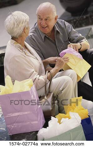 Stock Image - Senior couple sitting together looking into shopping bags. Fotosearch