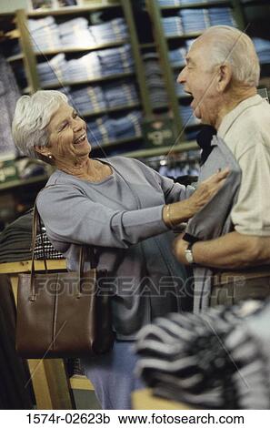 Stock Image - Senior woman holding a t-shirt against a senior man in a clothing store. Fotosearch