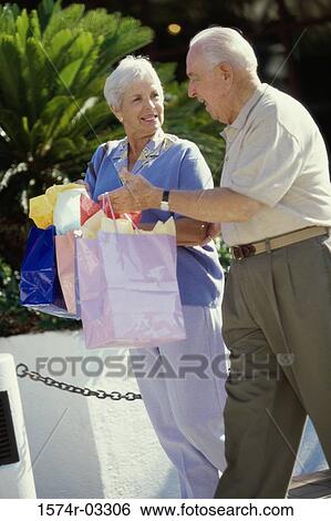 Stock Photograph - Side profile of a senior couple walking with shopping bags. Fotosearch