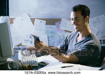 Stock Image - Side profile of a young man working on a computer holding a credit card. Fotosearch