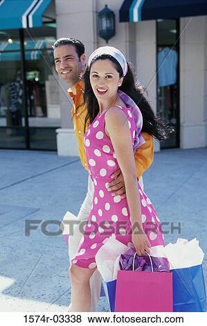 Stock Photo - Side profile of young couple walking with shopping bags. Fotosearch