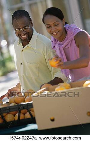 Stock Image - Young couple picking oranges from a shop in a market. Fotosearch