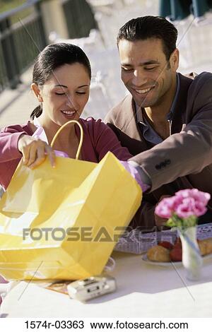Young couple sitting in a cafe looking into a shopping bag View Large Photo Image Stock Image - Young couple sitting in a cafe looking into a shopping bag. Fotosearch