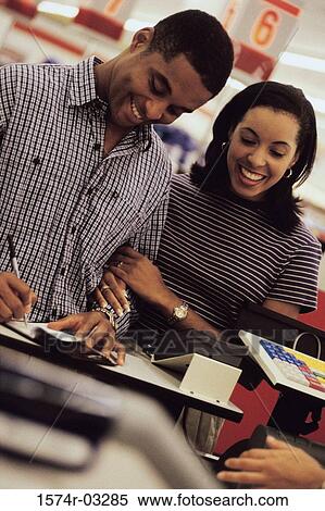 Stock Photography - Young couple standing in front of a checkout counter in a shopping mall. Fotosearch