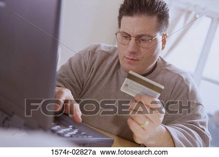 Young man sitting in front of a laptop holding a credit card View Large Photo Image Stock Image - Young man sitting in front of a laptop holding a credit card. Fotosearch