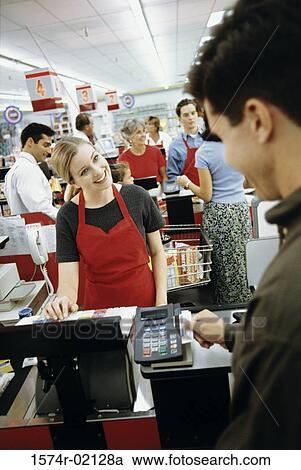 Stock Image - Young man using a credit card machine at a checkout counter in a supermarket. Fotosearch