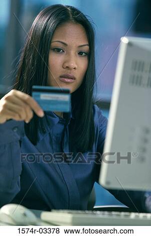 Young woman sitting in front of a computer holding a credit card View Large Photo Image Stock Photo - Young woman sitting in front of a computer holding a credit card. Fotosearch
