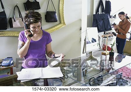 Stock Image - Young woman talking on a telephone in a store. Fotosearch