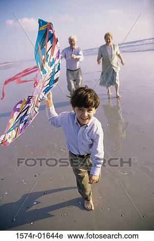 Stock Image - Boy flying a kite on the beach with his grandparents. Fotosearch