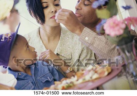 Stock Image - Close of a young couple eating pizza with their son. Fotosearch