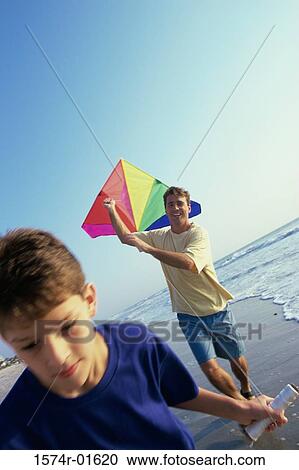Stock Image - Close-up of a boy flying a kite with his father on the beach. Fotosearch
