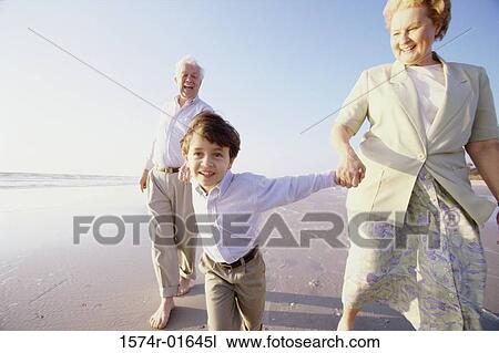 Stock Image - Close-up of a boy holding his grandparents hands on the beach. Fotosearch