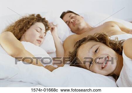 Stock Image - Close-up of a girl lying with her parents in bed. Fotosearch