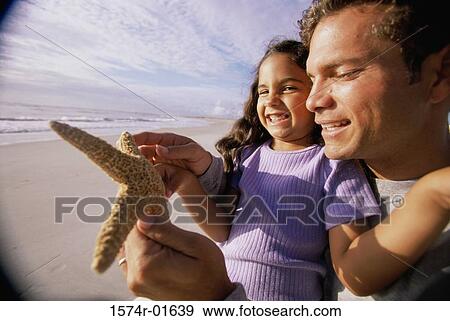 Stock Photo - Close-up of a man showing his daughter a starfish on the beach. Fotosearch