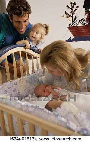Stock Image - Father and mother looking at their baby in a crib. Fotosearch