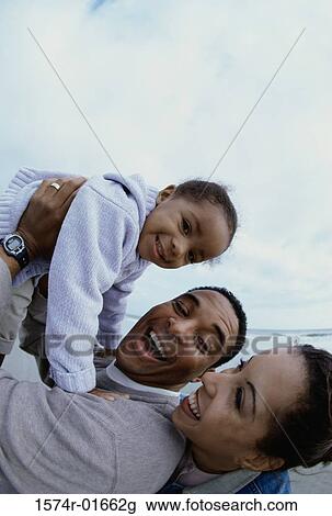 Stock Image - Father and mother together with their daughter at the beach. Fotosearch