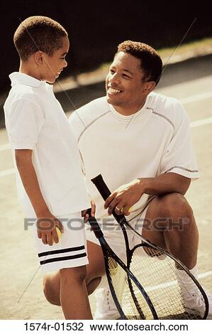 Stock Image - Father and son in tennis outfits holding rackets. Fotosearch