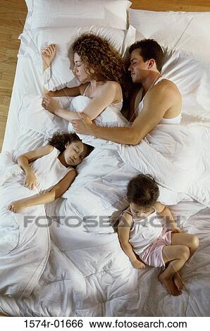 Stock Photograph - High angle view of a couple sleeping in bed with their daughters. Fotosearch