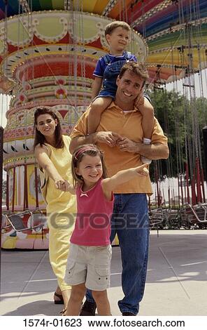 Parents and their two children walking in an amusement park View Large Photo Image Stock Image - Parents and their two children walking in an amusement park. Fotosearch