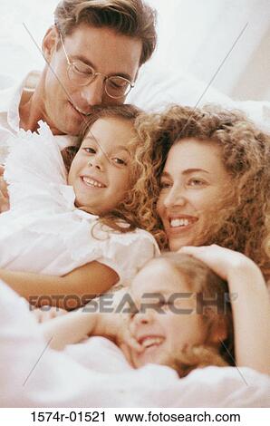 Stock Image - Parents and their two daughters together in bed. Fotosearch