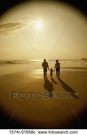 Stock Image - Silhouette of a father and a mother with their daughter at the beach. Fotosearch