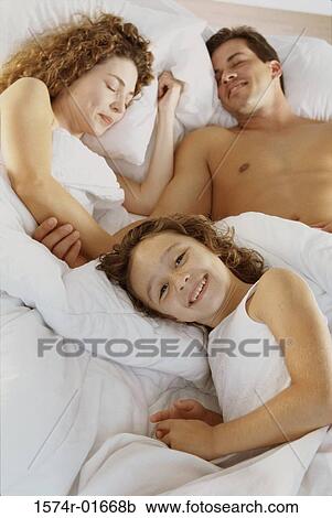 Stock Image - Young couple lying in bed with their daughter. Fotosearch